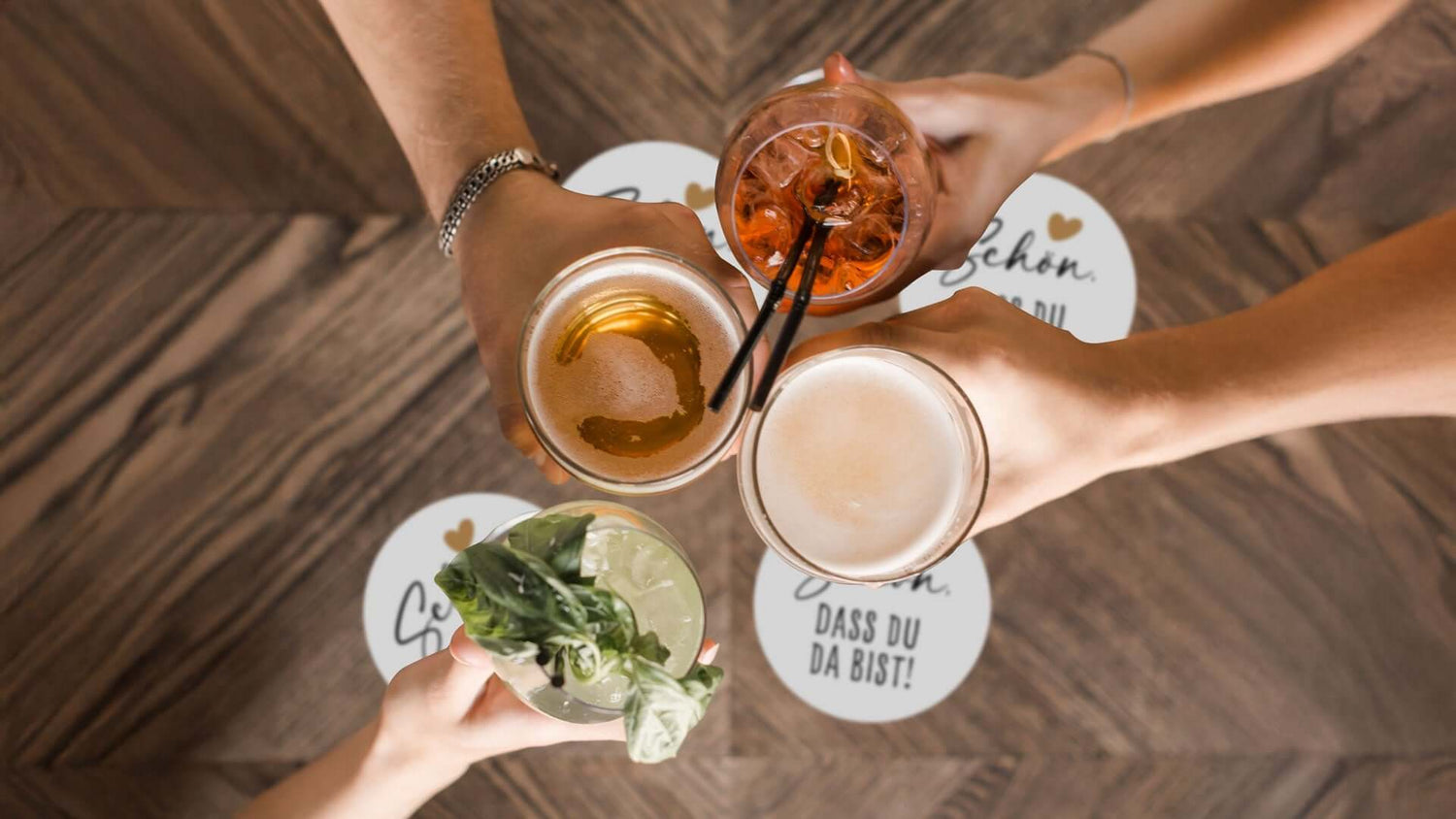 Hände halten Gläser mit Getränken über stilvollen Getränke-Untersetzern, ideal für Tischdeko bei Feiern.