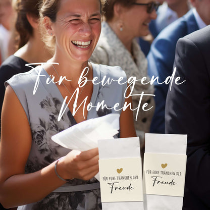 Lächelnde Frau mit Taschentüchern während einer Hochzeit, umgeben von Gästen, mit Fokus auf Taschentuch-Banderolen.